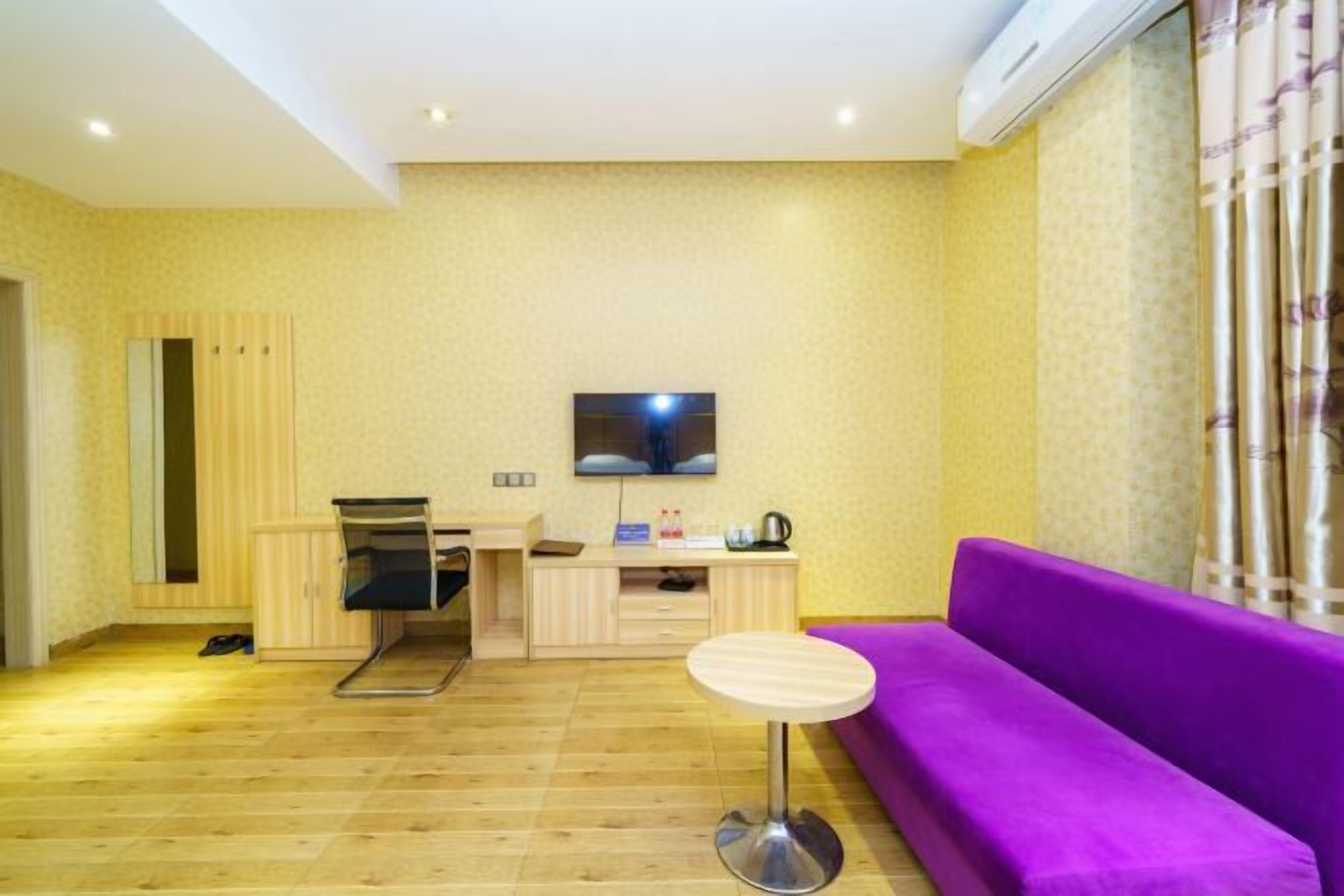 A room with a wooden floor, a purple sofa, a small round table, a TV mounted on the wall, and a cabinet.