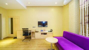 A room with a wooden floor, a purple sofa, a small round table, a TV mounted on the wall, and a cabinet.