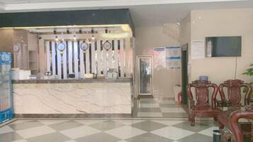 A hotel reception area with a marble counter, wooden chairs, and a check-in desk.