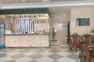 Zona de recepción de un hotel con mostrador de mármol, sillas de madera y un mostrador de registro.