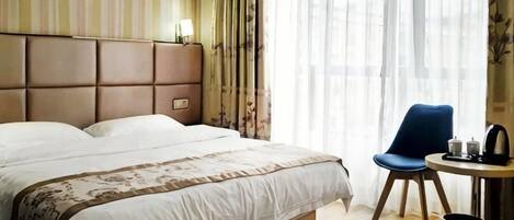 A hotel room with a large bed, a chair, a small table, and a window with curtains.