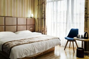 A hotel room with a large bed, a chair, a small table, and a window with curtains.