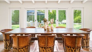 A dining area with a wooden table and chairs, large windows, and a view of the outdoors. - Historical 1937 Movie Colony Spanish Hacienda (Palm Springs)