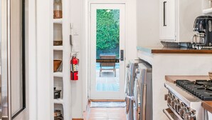 A narrow kitchen with a tiled floor, stainless steel appliances, and a view into a dining area. - Historical 1937 Movie Colony Spanish Hacienda (Palm Springs)