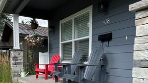 En veranda med to Adirondack-stole, en rød og en grå, samt en blomsterkasse hængt op.