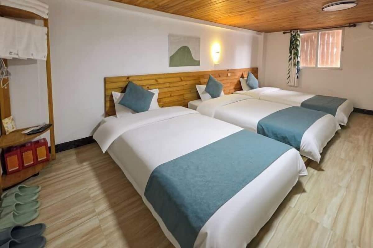 Hotelkamer met twee bedden, een houten hoofdbord, een wandlamp, een raam met gordijnen en een schoenenrek.