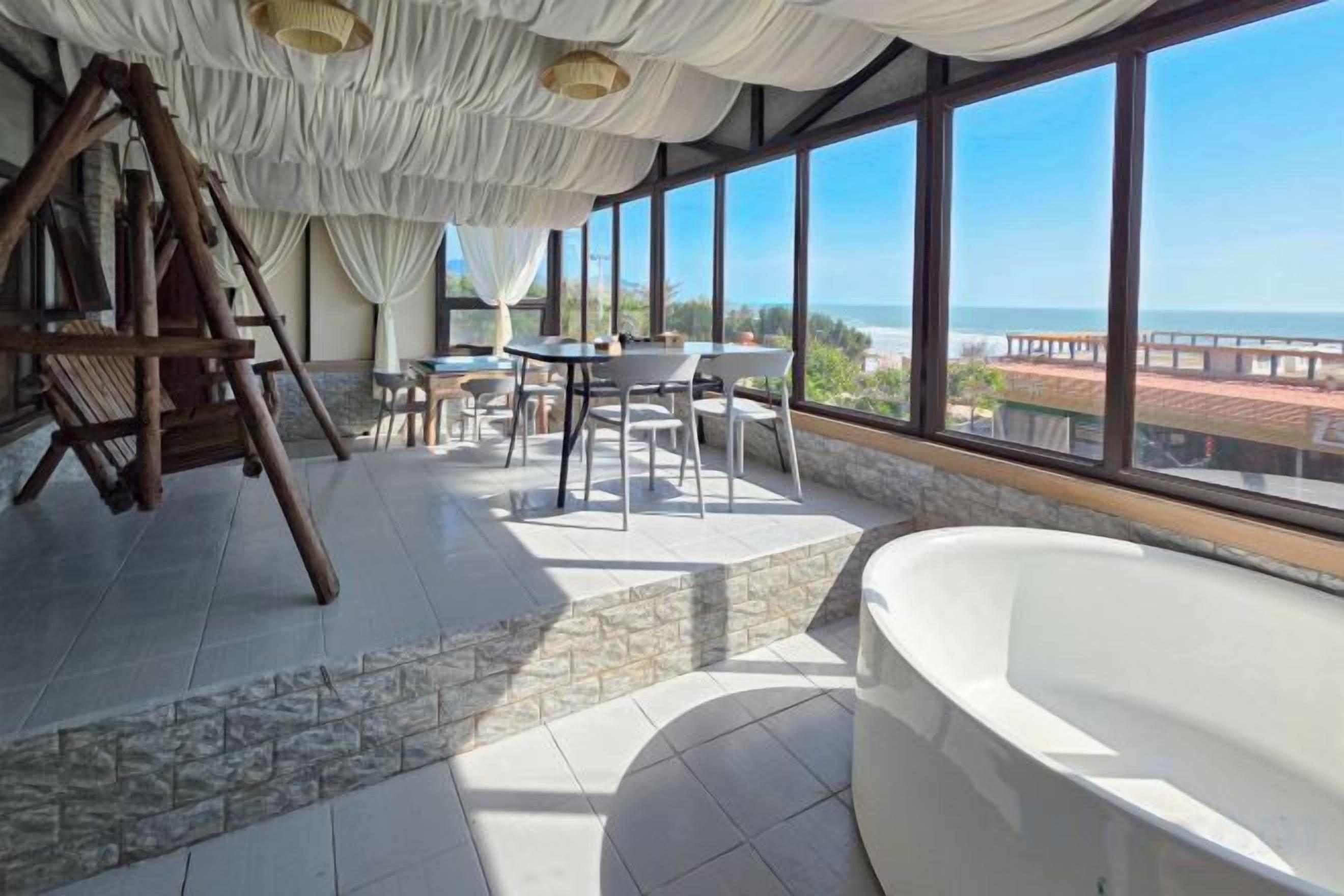 A room with a large window, a bathtub, and a wooden swing.