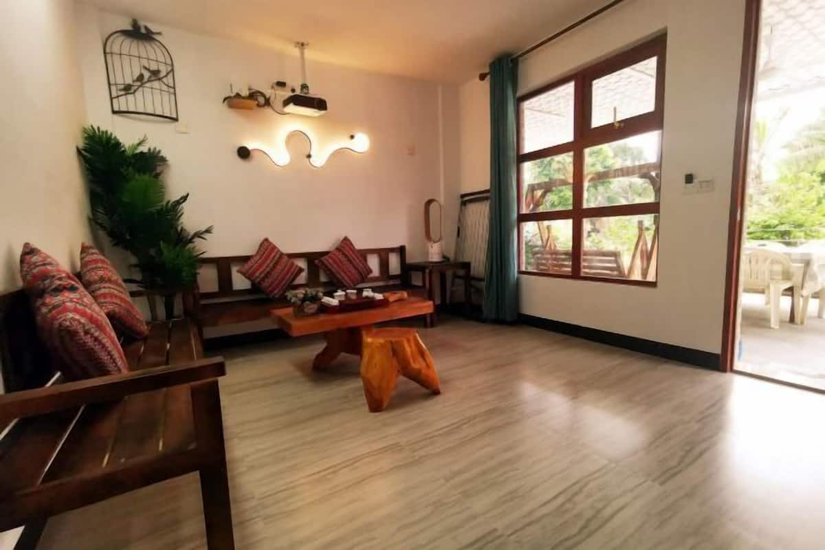 Een gezellige woonkamer met een houten bank, een bijzettafeltje en een groot raam met gordijnen.