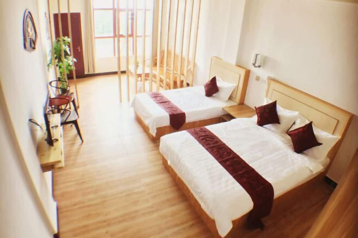 Een hotelkamer met twee bedden, houten vloeren, een bureau met stoel en een groot raam.