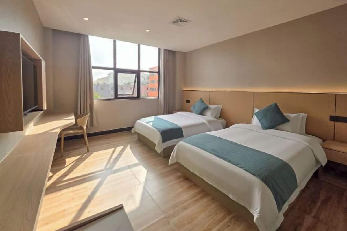 Een hotelkamer met twee bedden, een televisie, een bureau en een raam met uitzicht op de stad.