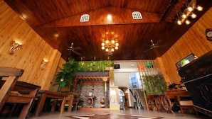 A wooden interior with a central chandelier, wooden benches, and a staircase leading to an upper level.