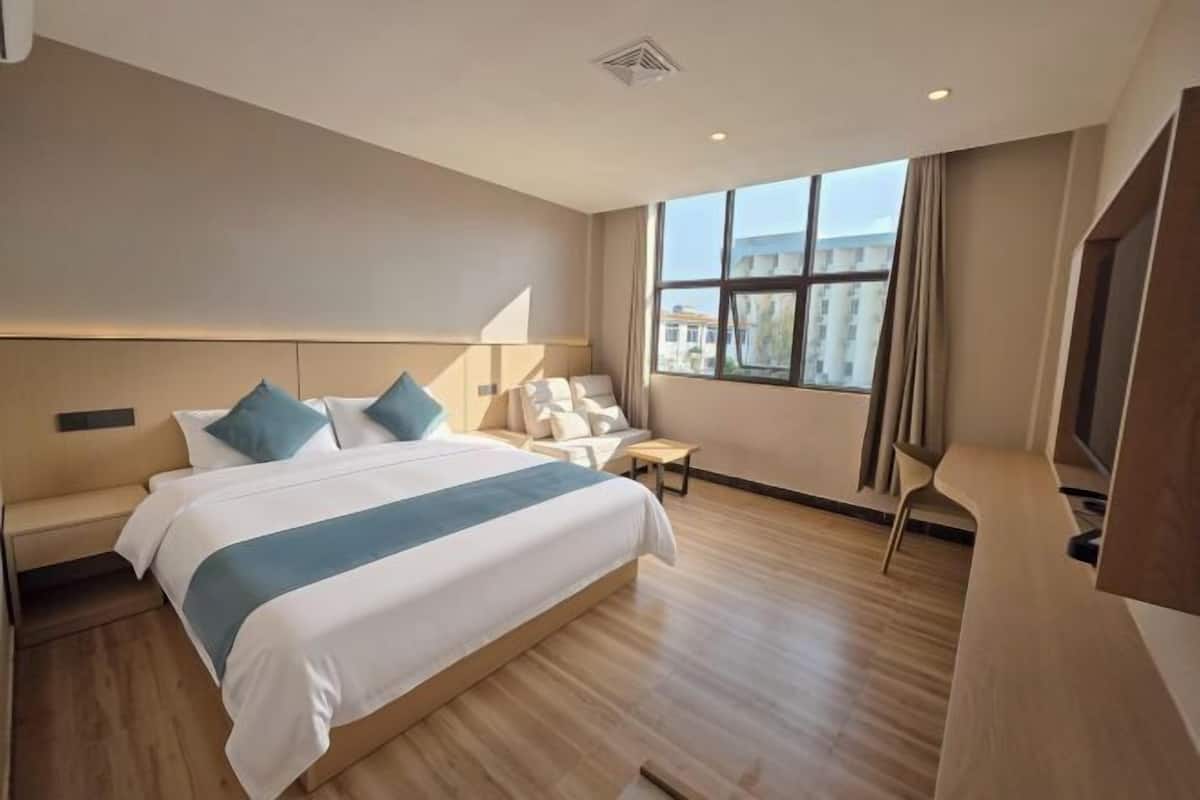 Een hotelkamer met een groot bed, een zithoek, een televisie en een raam met uitzicht op gebouwen.