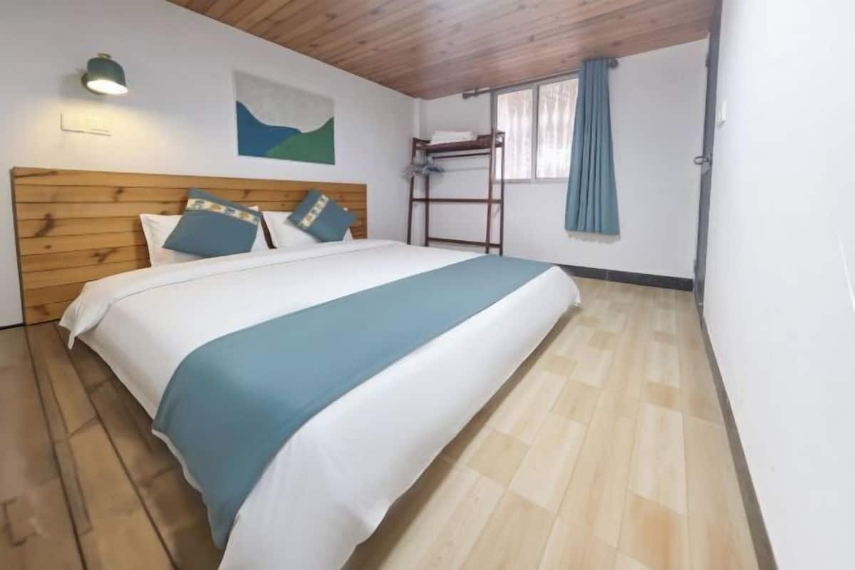 Een slaapkamer met een stapelbed, een houten hoofdeinde, een bed met wit en teal beddengoed, een wandlamp, een raam met gordijnen en een houten vloer.