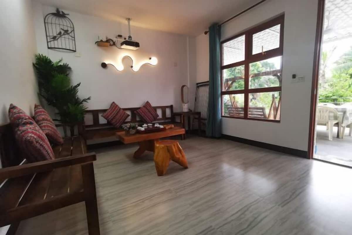 Een kamer met een houten bankje, een kleine tafel, een vogelkooi decoratie en een groot raam.