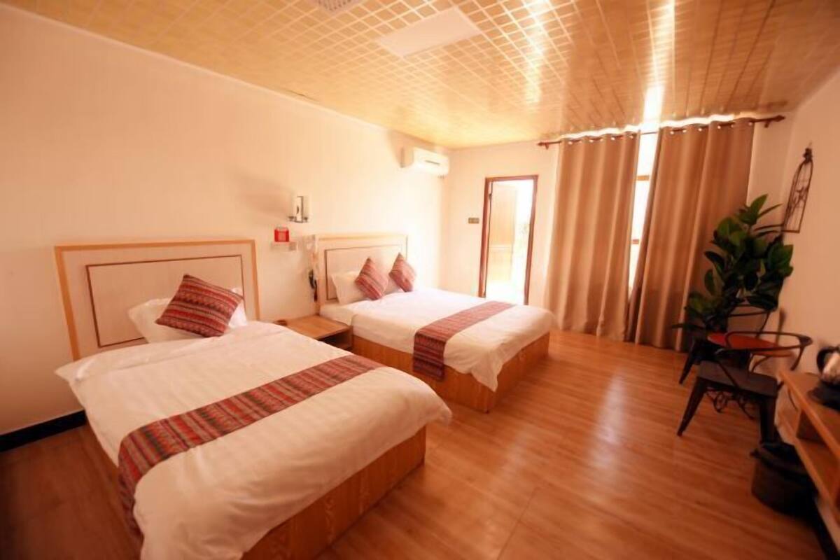 Een hotelkamer met twee bedden, houten vloeren, een plafondventilator en een potplant.