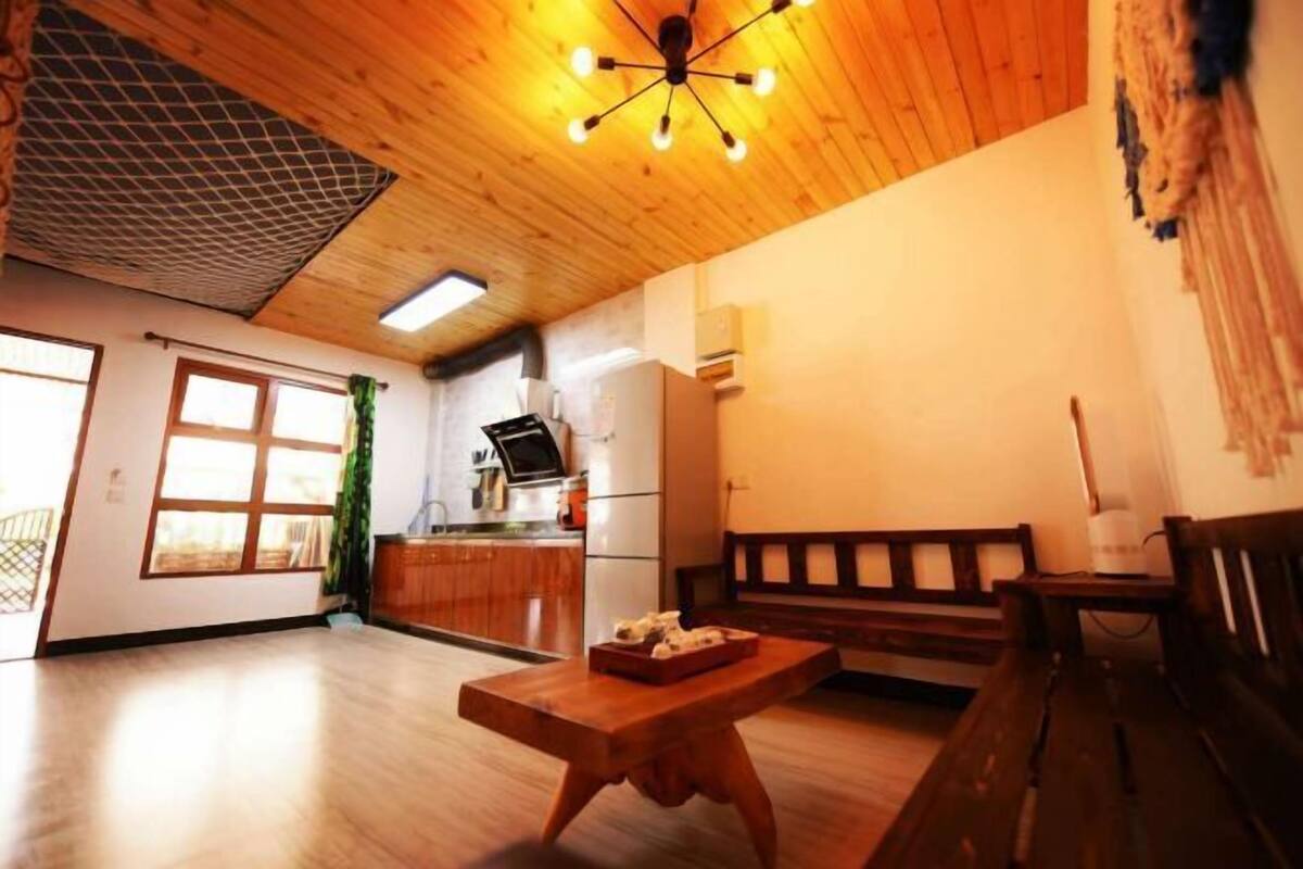 Ruime kamer met houten plafond, een eettafel, een bank en een keuken met een koelkast en fornuis.