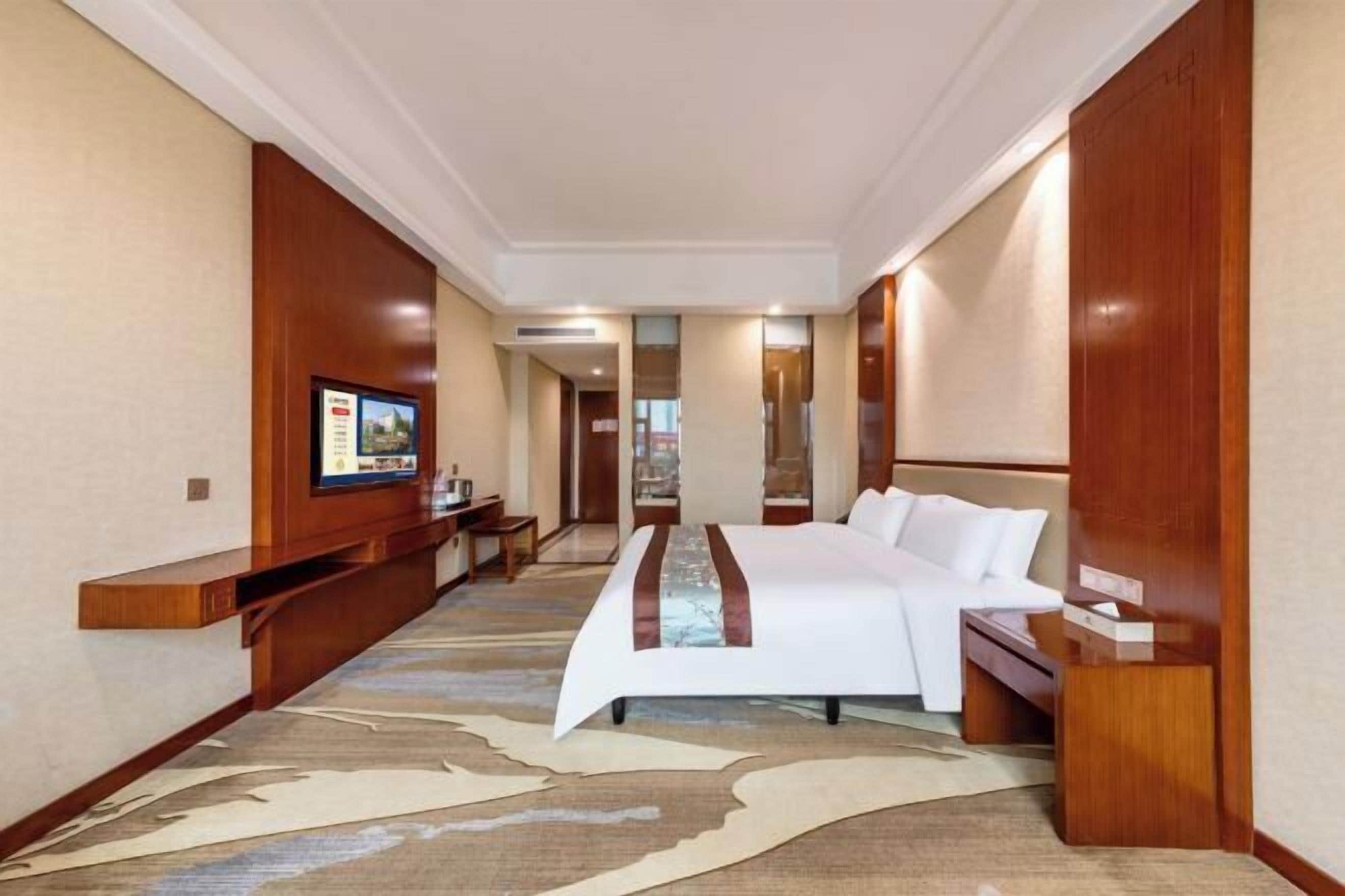 A hotel room with a bed, a TV, a desk, and a mirror.