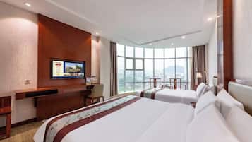 Quarto de hotel com duas camas, uma escrivaninha, televisão e uma janela grande com vista para a cidade.