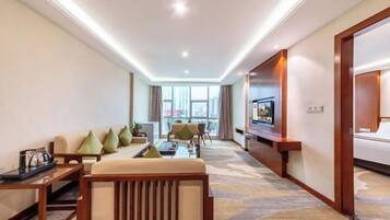A hotel room with a sofa, armchairs, a coffee table, a TV, and a large window.