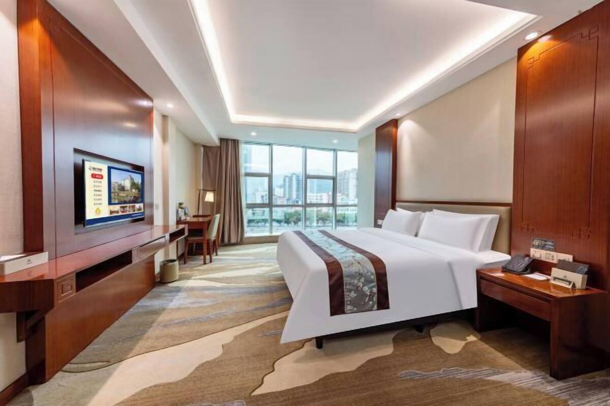 A hotel room with a large bed, a desk with a chair, a television, and a view of the city.