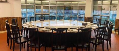 A conference room with a round table and chairs, large windows with a city view, and a high ceiling with recessed lighting.
