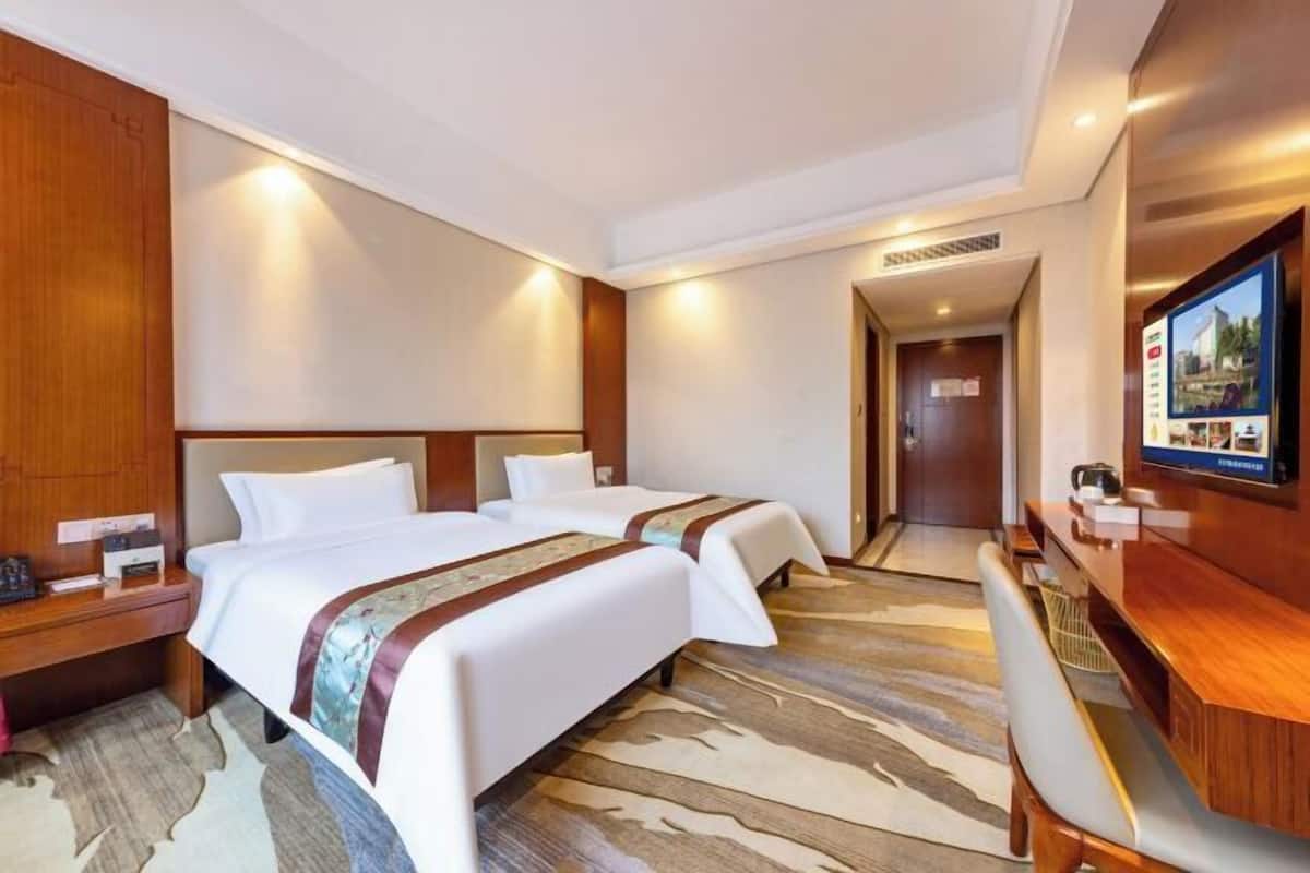 A hotel room with two beds, a desk, a TV, and a wooden wardrobe.