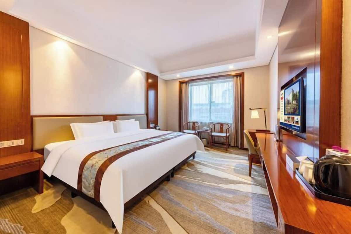 A hotel room with a large bed, a desk, a chair, a television, and a window with curtains.