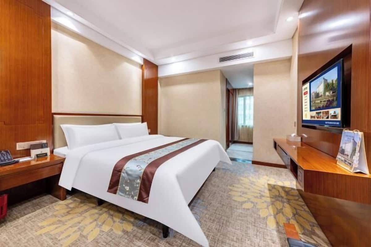 A hotel room with a large bed, a desk with a computer, a television, and a reception desk.