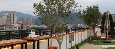 An outdoor bar area with seating, a view of a cityscape, and a tree.