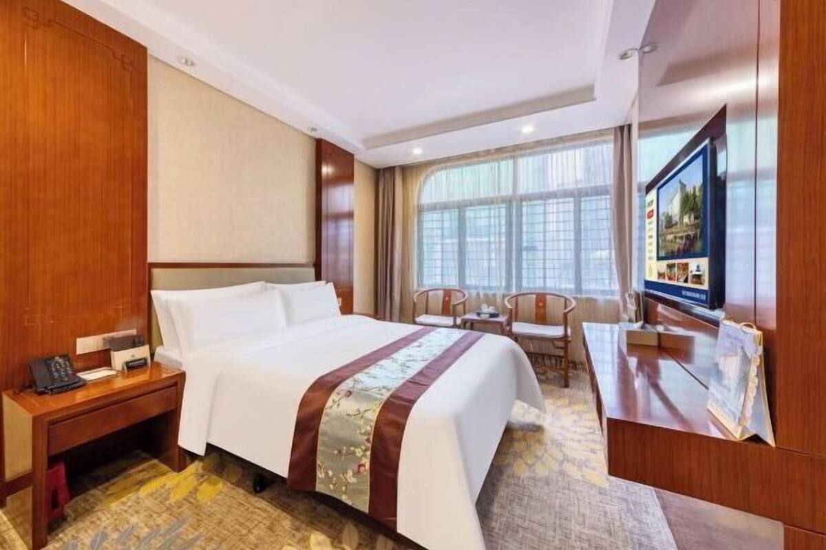 A hotel room with a bed, bedside table, TV, and a desk with chairs.
