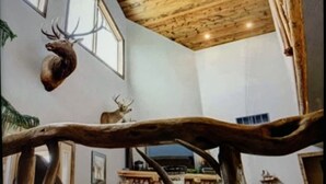 A room with wooden ceiling beams, a mounted deer head on the wall, and a tree branch decoration. - Cozy Cabin with Beautiful Views. Minutes from Downtown Custer (Custer)