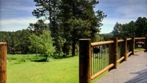 A wooden deck with a metal railing overlooking a grassy area with trees. - Cozy Cabin with Beautiful Views. Minutes from Downtown Custer (Custer)