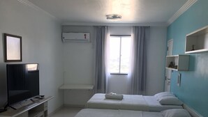 Quarto de hotel com duas camas, televisão, janela com cortinas e ventoinha no teto.