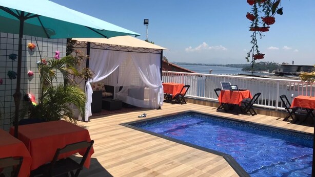 Uma piscina no terraço com vista para o mar, área de estar coberta e uma mesa com um laptop.