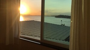 Quarto com uma grande janela com vista para a água durante o pôr do sol.