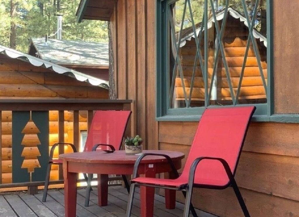 Uma cabana de madeira com varanda, uma mesa e duas cadeiras vermelhas.
