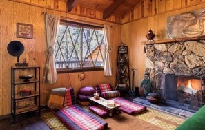 L’intérieur chaleureux d’un chalet avec une cheminée en pierre, des murs en bois et un coin salon confortable agrémenté de coussins.