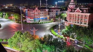 A nighttime view of a roundabout with buildings featuring traditional architecture, surrounded by greenery and street lighting. - Shangshi Hotel (Fuyun)