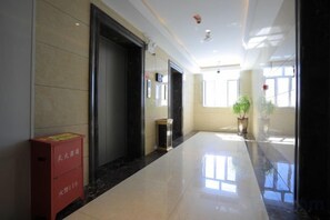 A hotel corridor with a shiny floor, a red box, and a potted plant. - Shangshi Hotel (Fuyun)