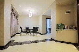 Un vestíbulo de hotel con piso de mármol, un mostrador de recepción, una zona de comedor con sillas y una planta en maceta.