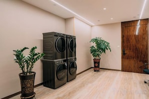 A laundry room with a large washer and dryer, two potted plants, and a wooden door. - Shangshi Hotel (Fuyun)