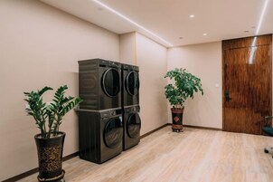Un lavadero con lavadora y secadora grandes, dos plantas en macetas y una puerta de madera.