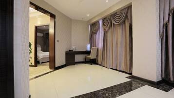Quarto de hotel com uma cama, uma escrivaninha e uma janela grande com cortinas.