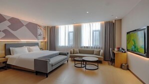 A modern hotel room with a bed, sofa, two small tables, a desk, and a TV. - Shangshi Hotel (Fuyun)
