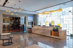 A hotel reception area with a marble counter, a seating area, and a large window with geometric patterns. - Shangshi Hotel (Fuyun)