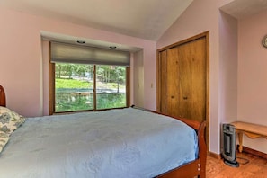 Une chambre avec un grand lit, une armoire en bois, un radiateur et une fenêtre donnant sur un paysage verdoyant.