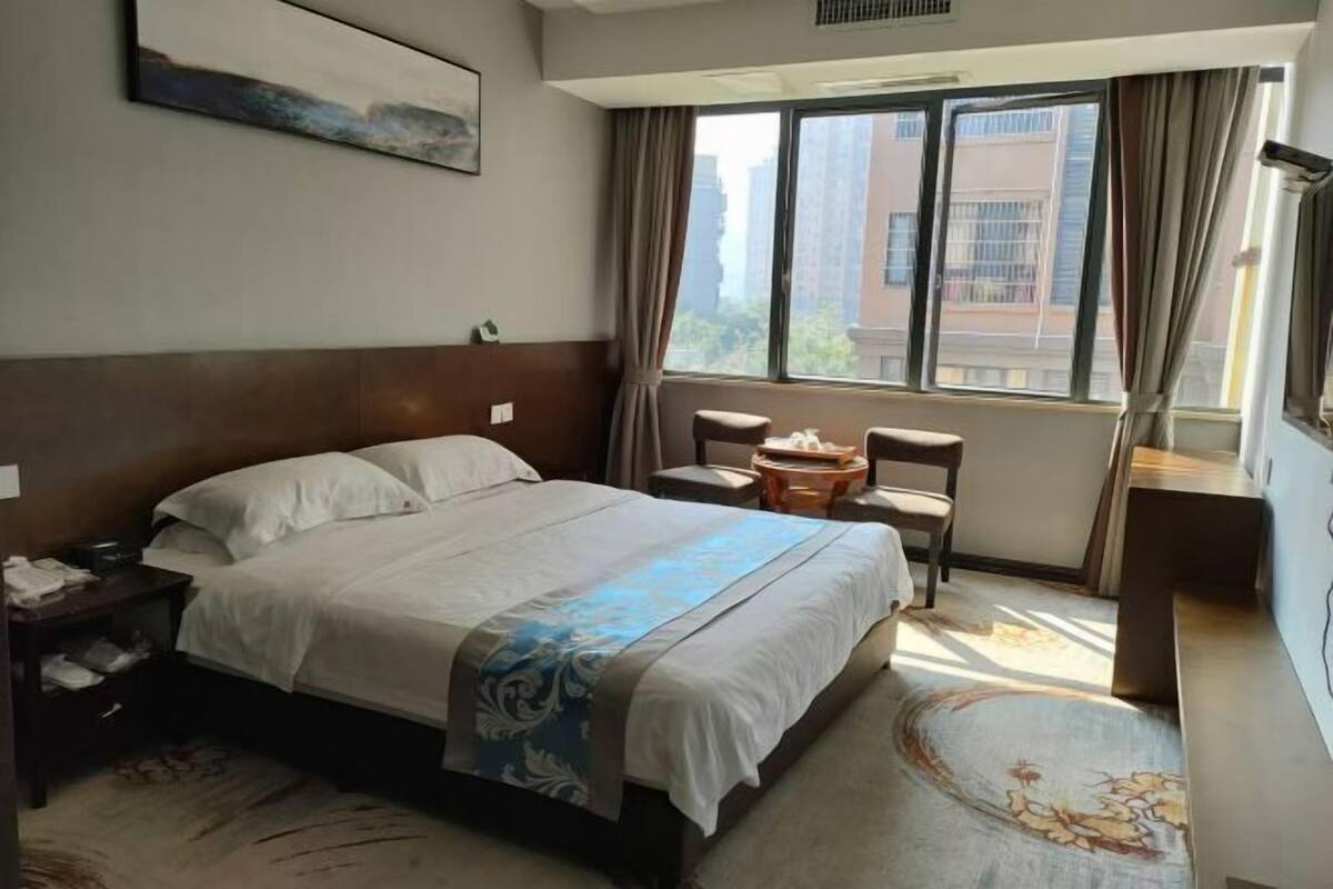 A hotel room with a large bed, a desk, a chair, and a window with curtains.