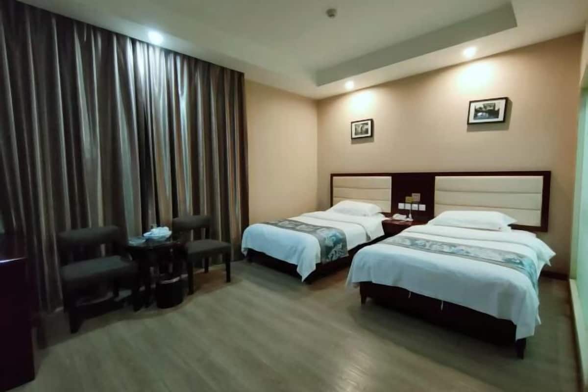 A hotel room with two beds, a desk, chairs, and a curtain.