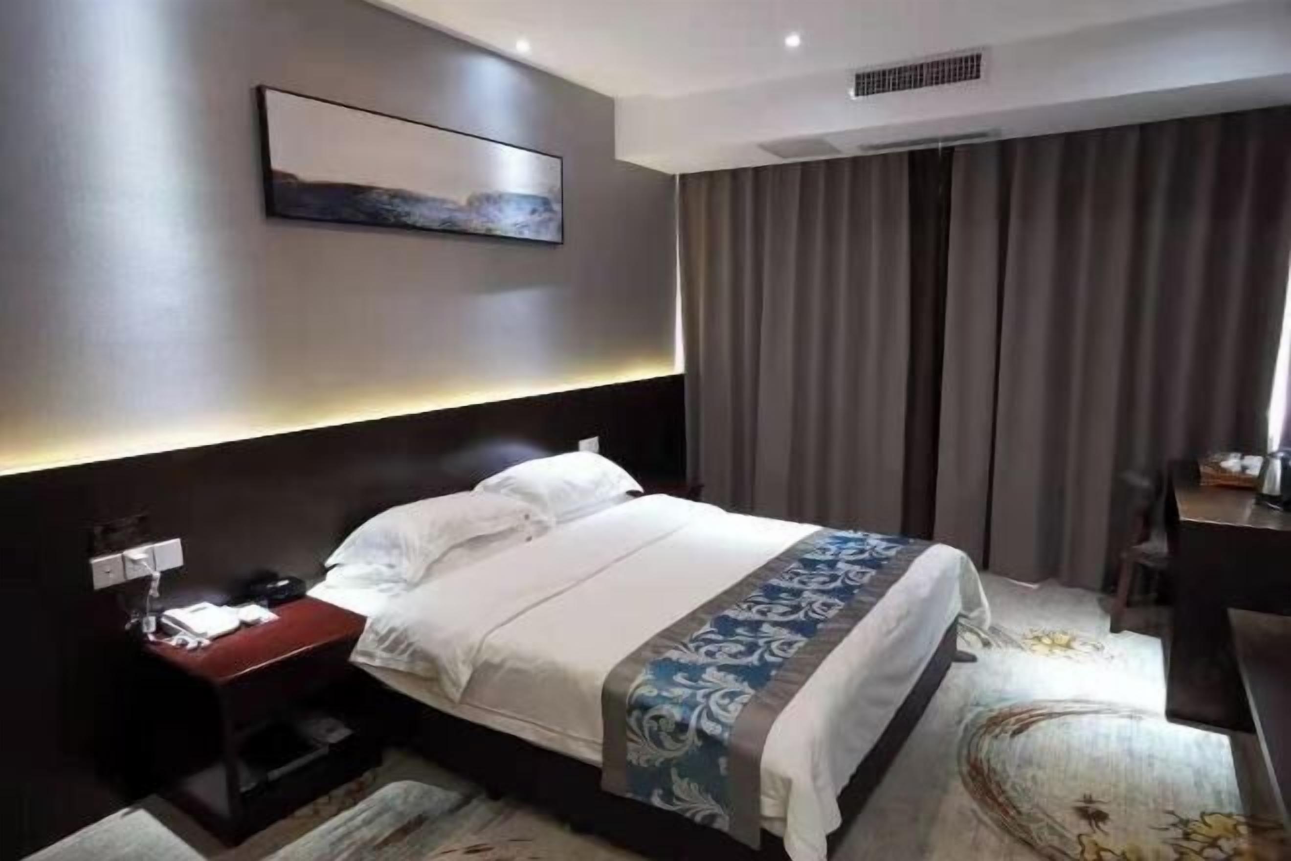 Una habitación de hotel con una cama, mesita de noche y un cuadro en la pared.