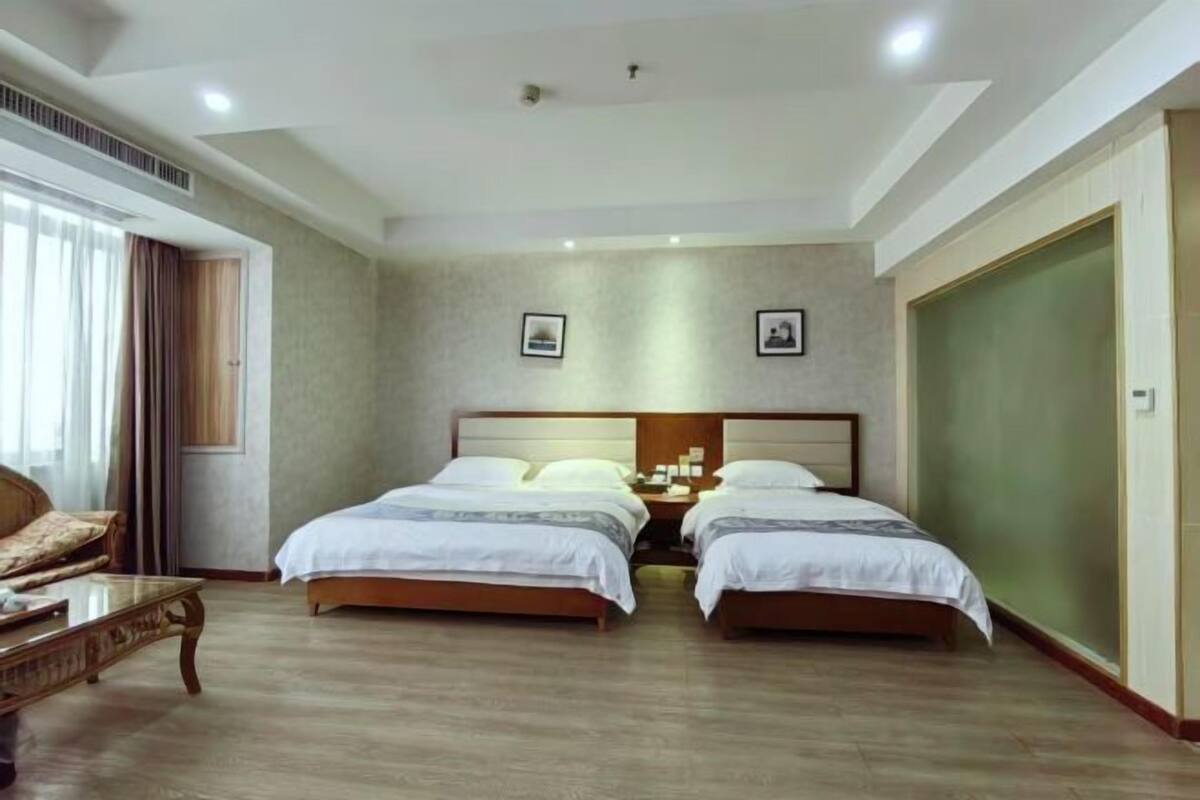 A hotel room with two beds, a sofa, a wooden coffee table, and a large wardrobe.